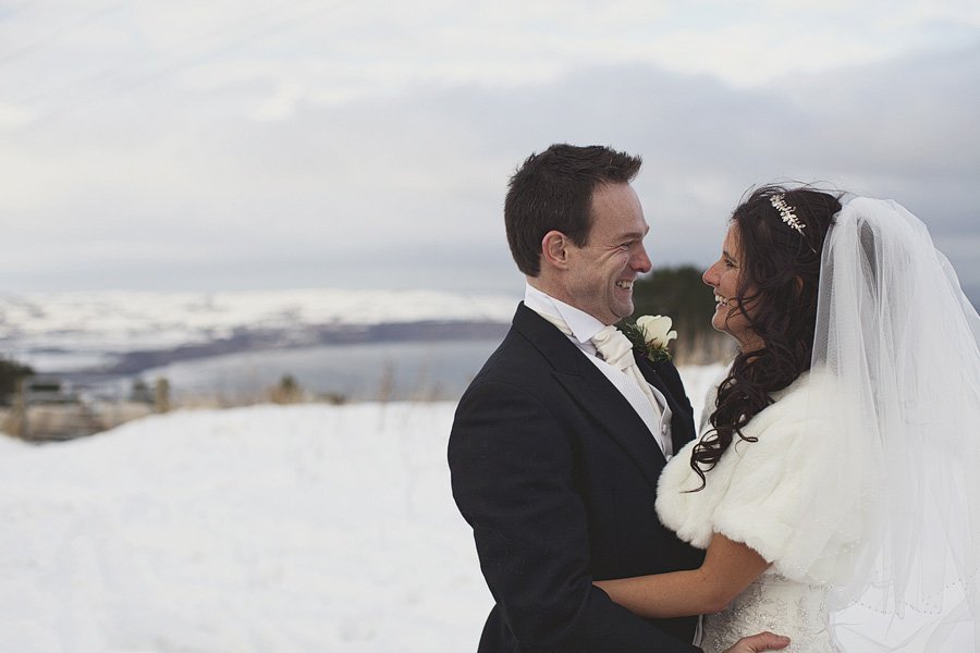 Bride and groom smiling in snowy coastal setting