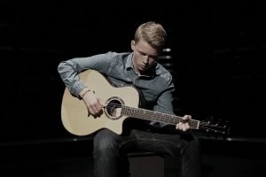 Young man playing acoustic guitar on dark stage