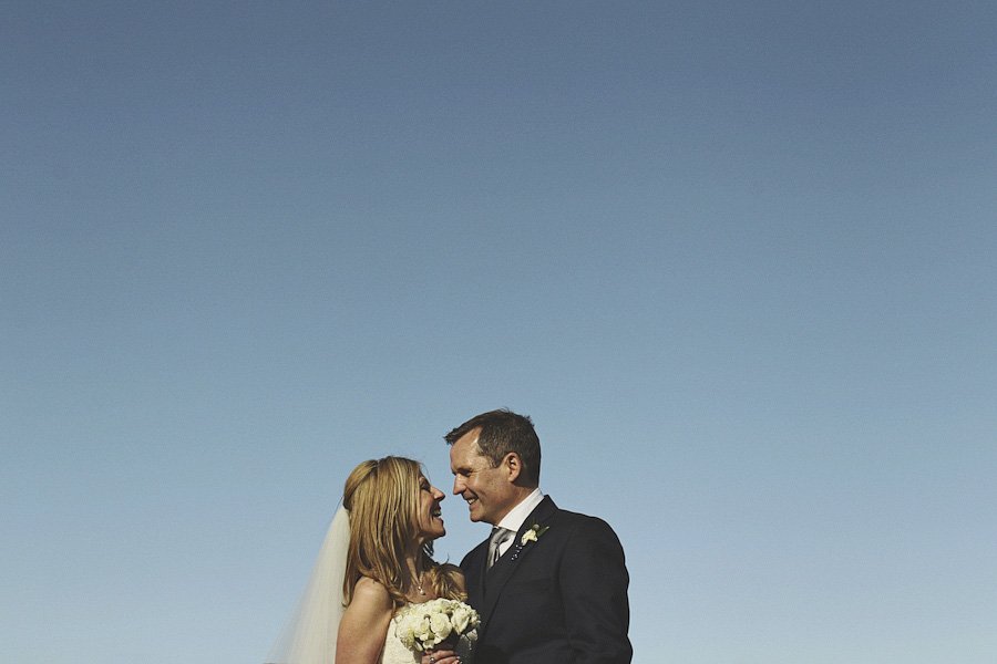 Bride and groom smiling under clear blue sky