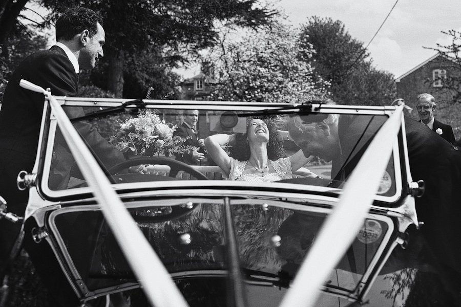 Bride laughing in vintage convertible on wedding day