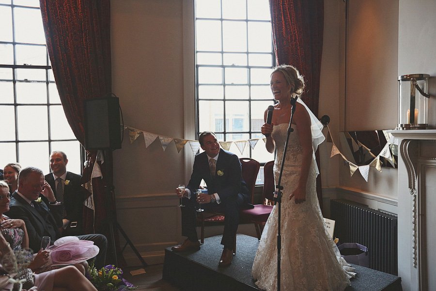 Bride giving wedding speech with groom smiling nearby