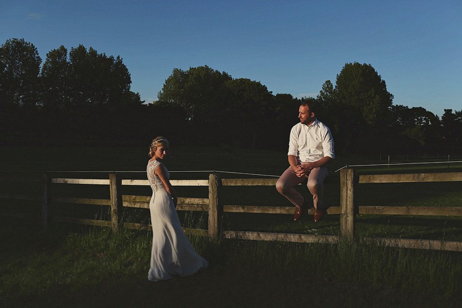 Bride and groom by wooden fence at sunset