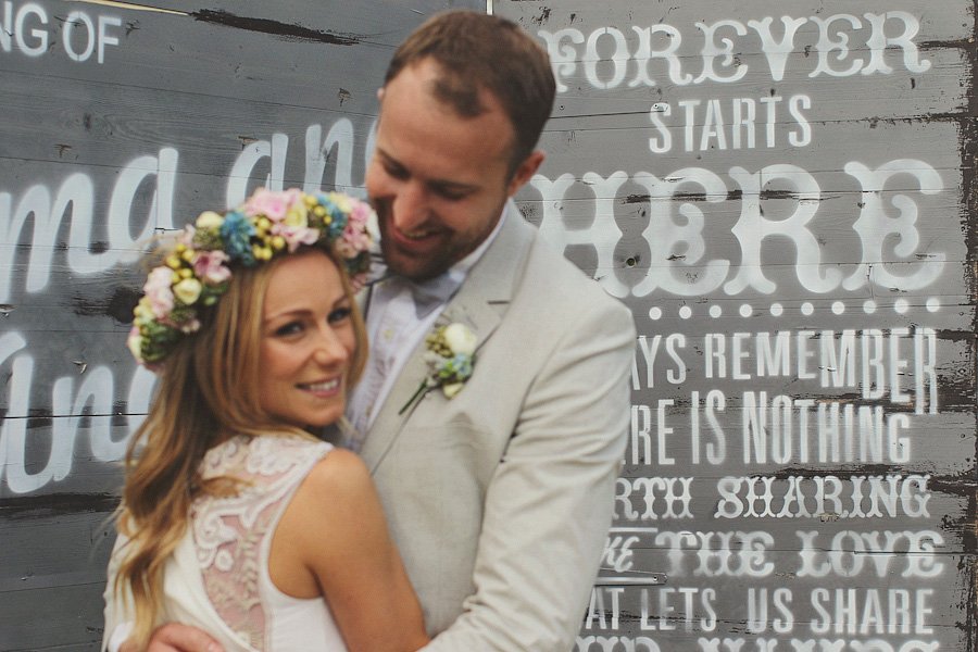 Bride and groom embracing before rustic wedding backdrop