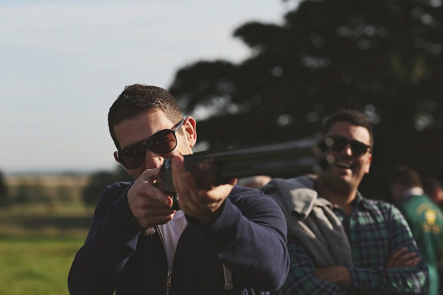 Man aiming shotgun outdoors with friend behind