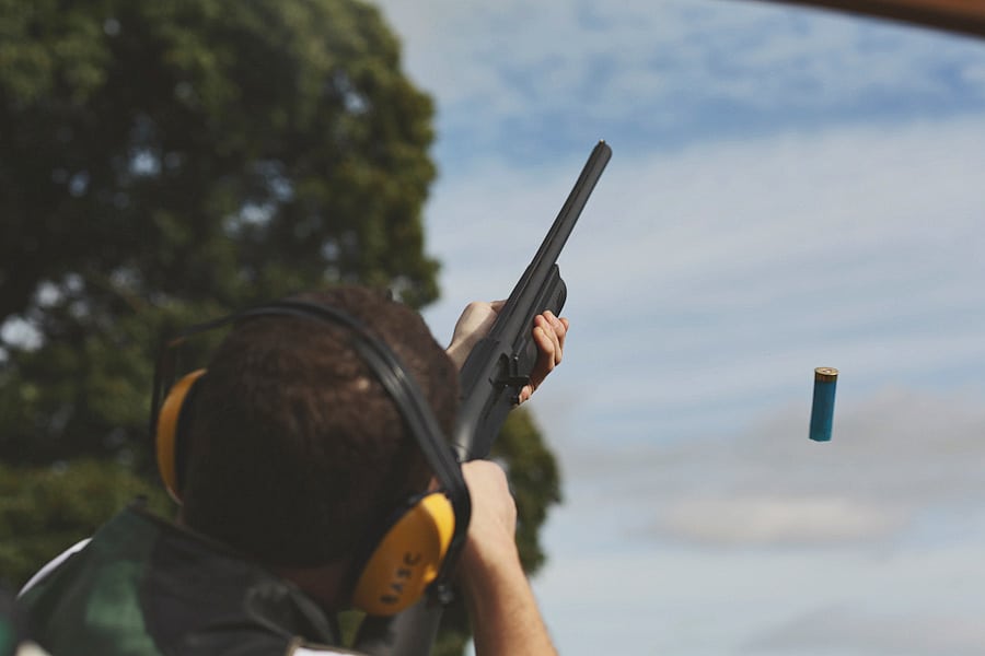 Person firing shotgun outdoors with shell ejecting