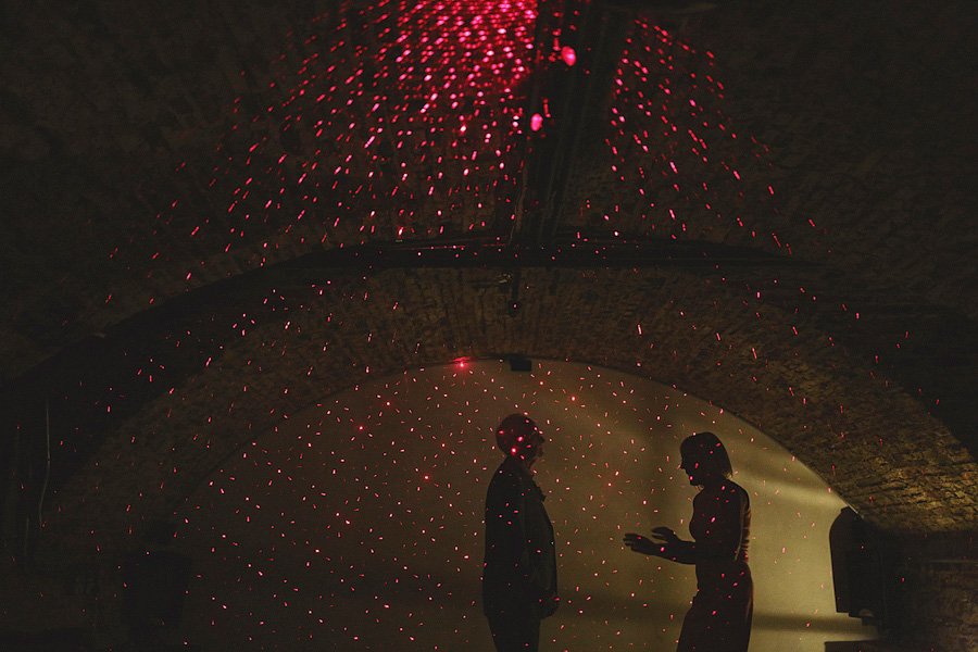 Two silhouettes under red laser lights indoors