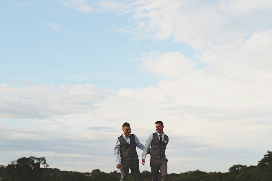 Two grooms walking outdoors under cloudy sky