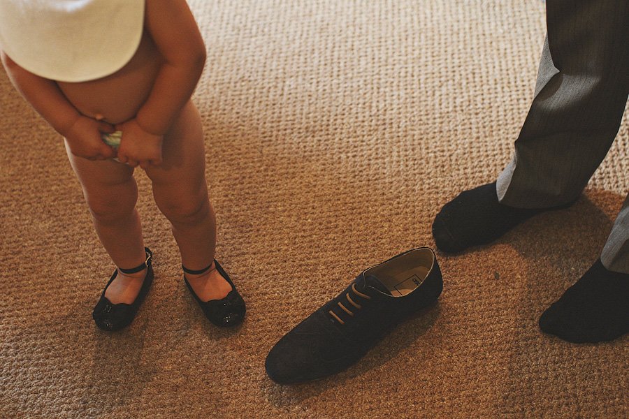 Toddler standing beside adult shoe on carpet