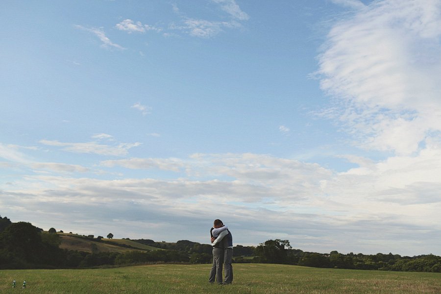 Couple hugging in open field under vast sky