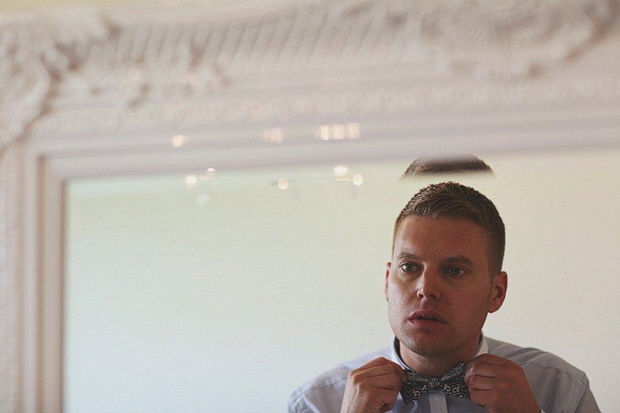 Man adjusting bow tie in mirror