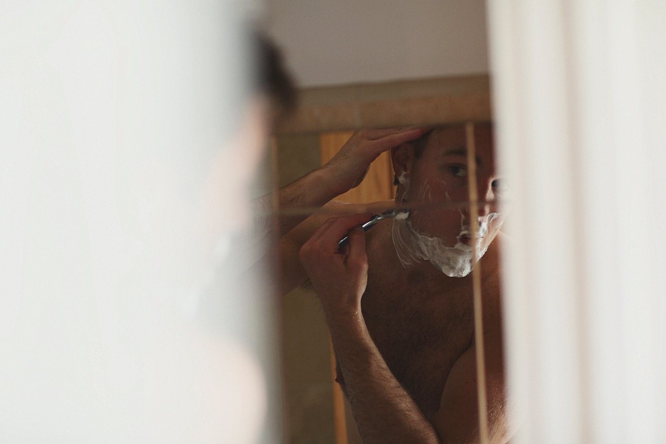 Man shaving face in shower reflection