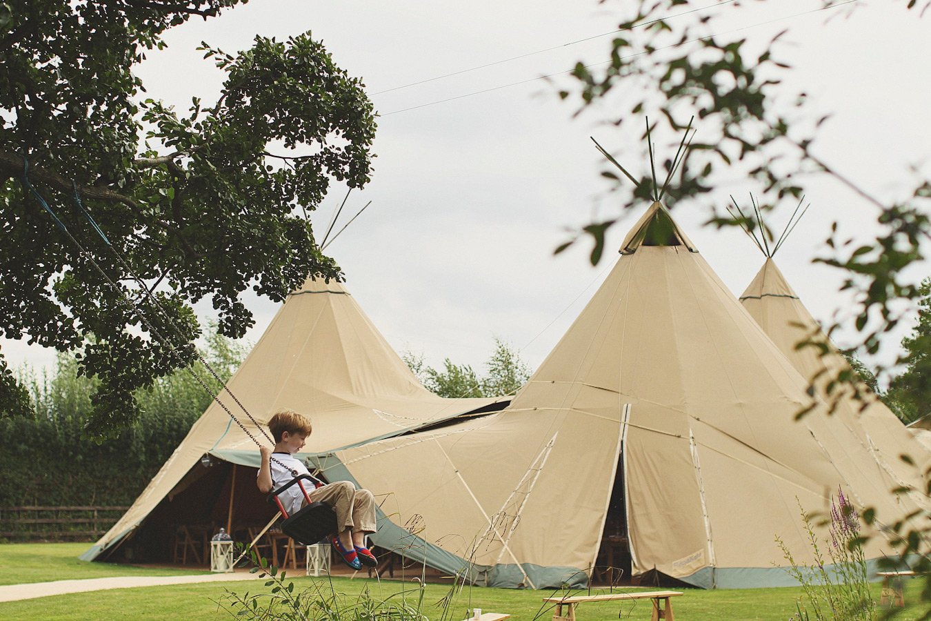 Child swinging beside large canvas glamping tents