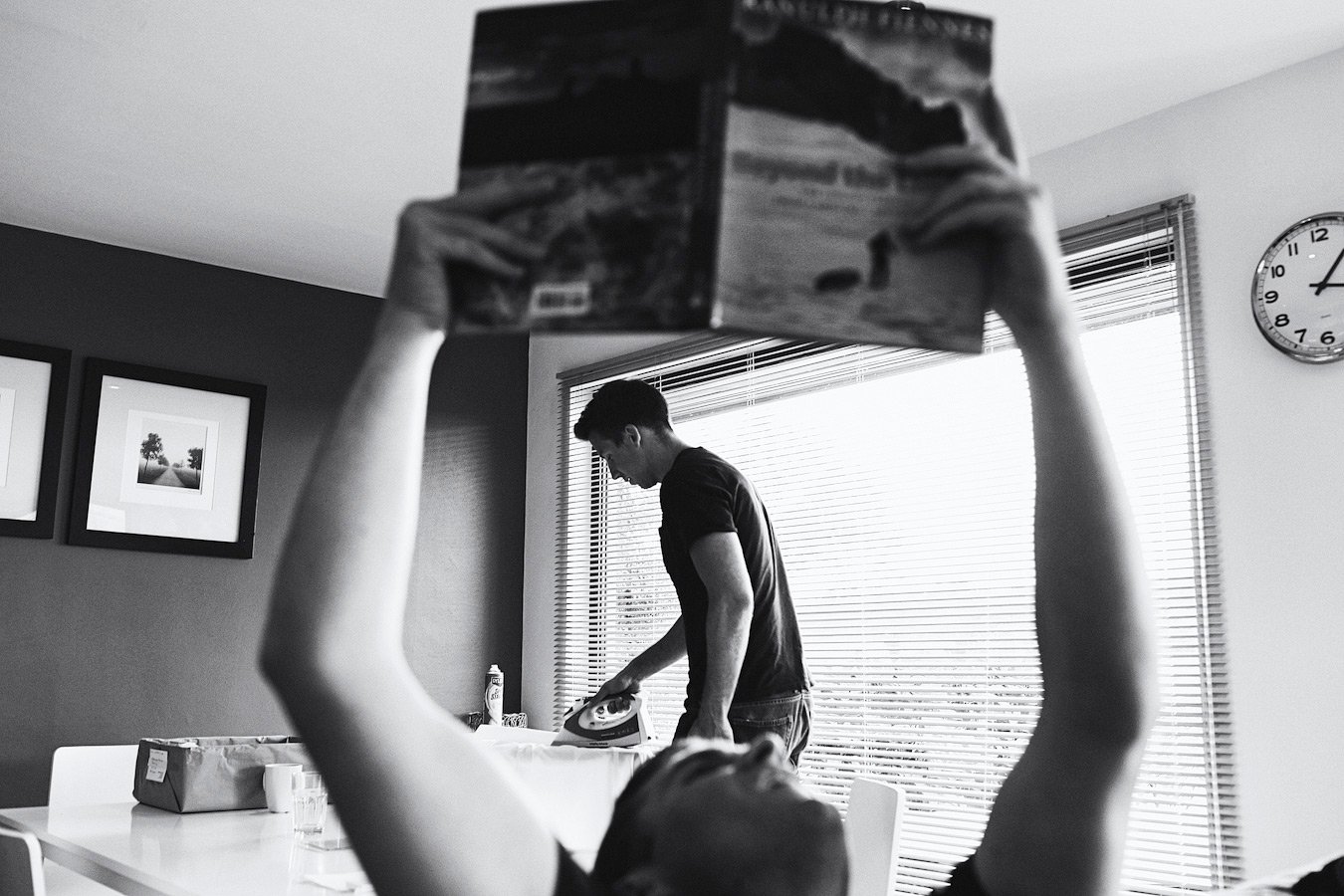 Man ironing while person reads magazine indoors