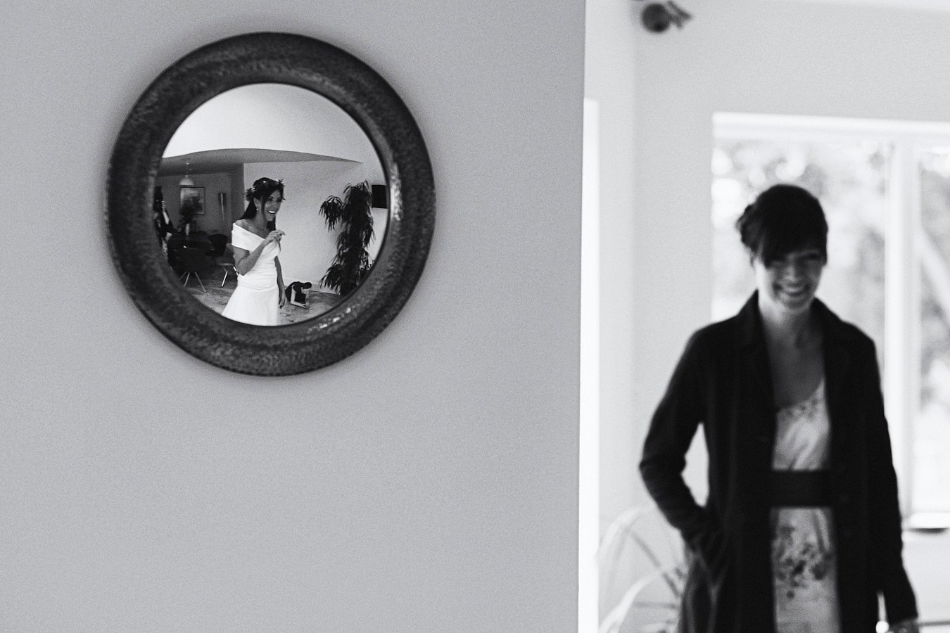 Bride reflected in round mirror, woman blurred foreground