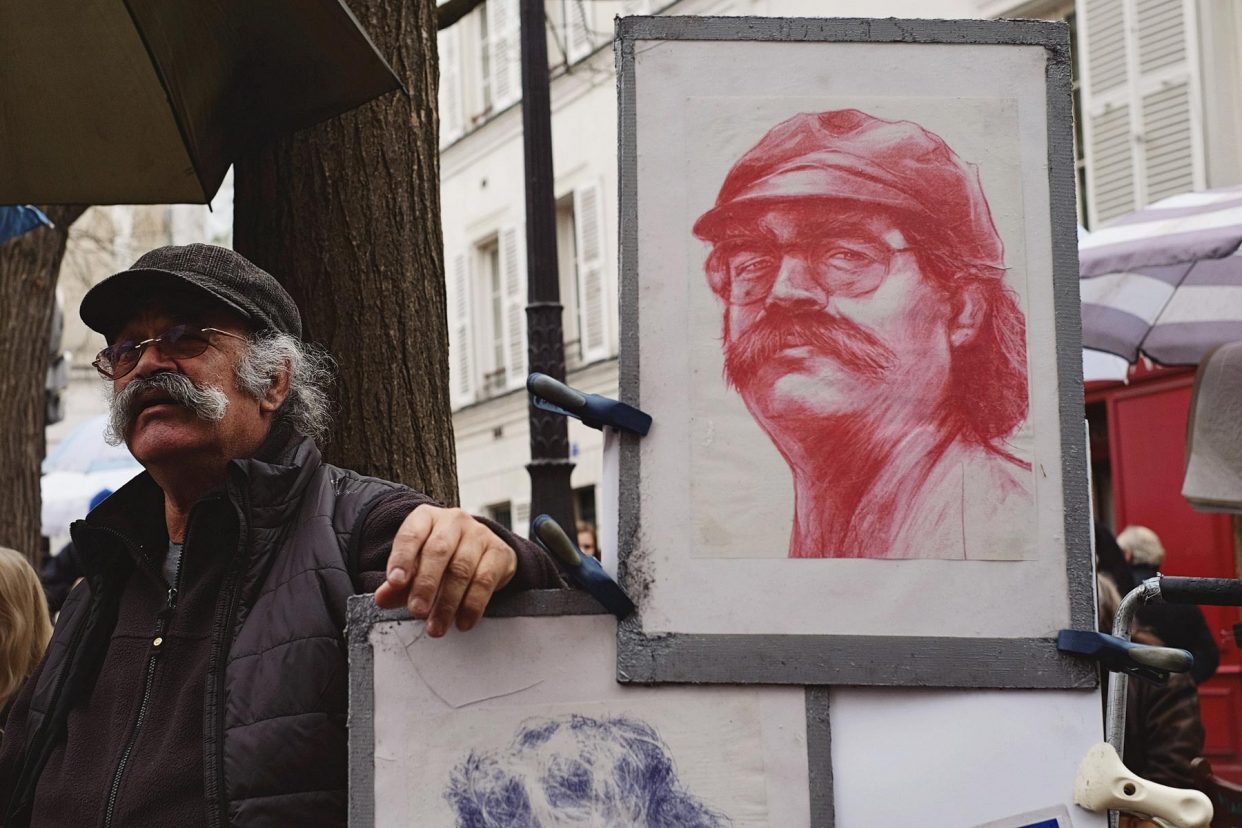 Street artist beside red portrait drawing