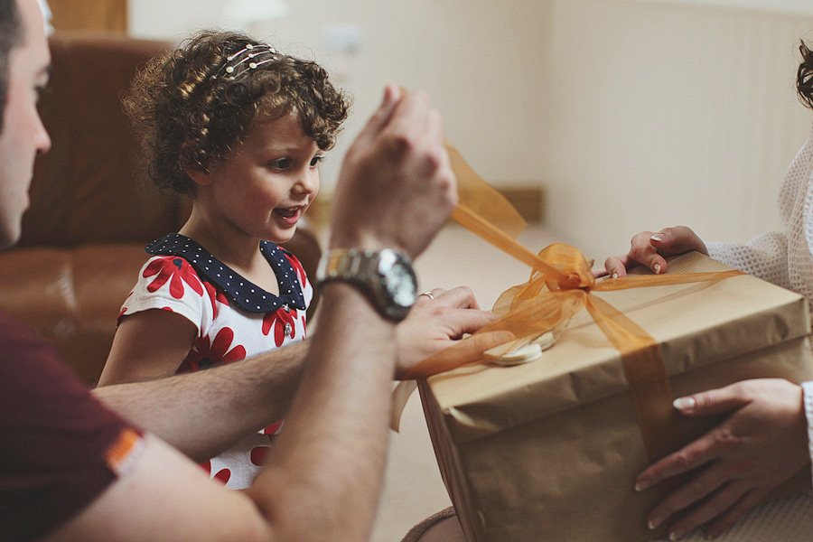 Young girl opening wrapped gift with parents