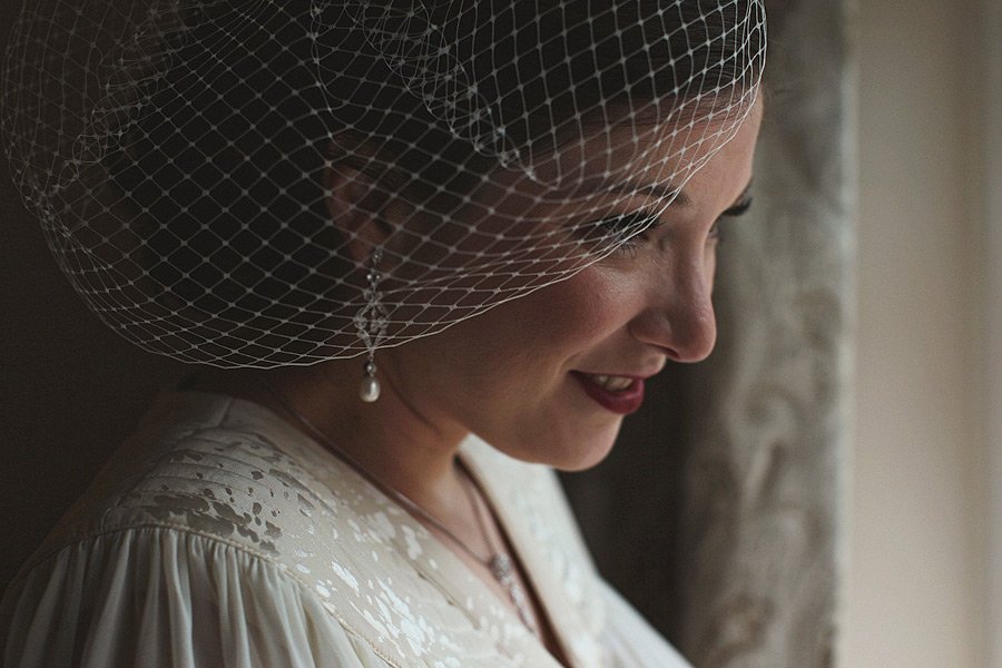 Bride wearing birdcage veil smiling by window
