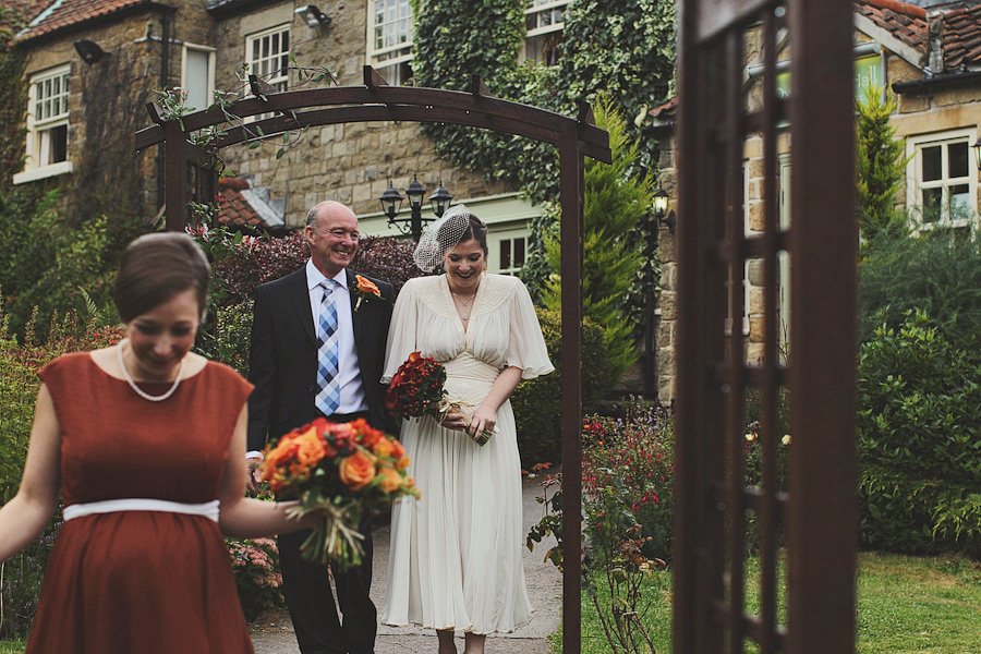 Bride walking with father under garden arch