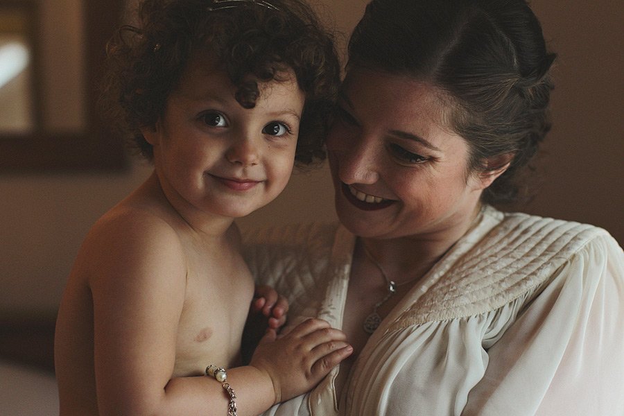 Woman holding smiling curly-haired toddler indoors