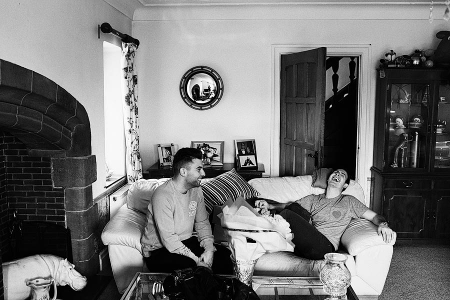 Two men laughing on couch with dog nearby