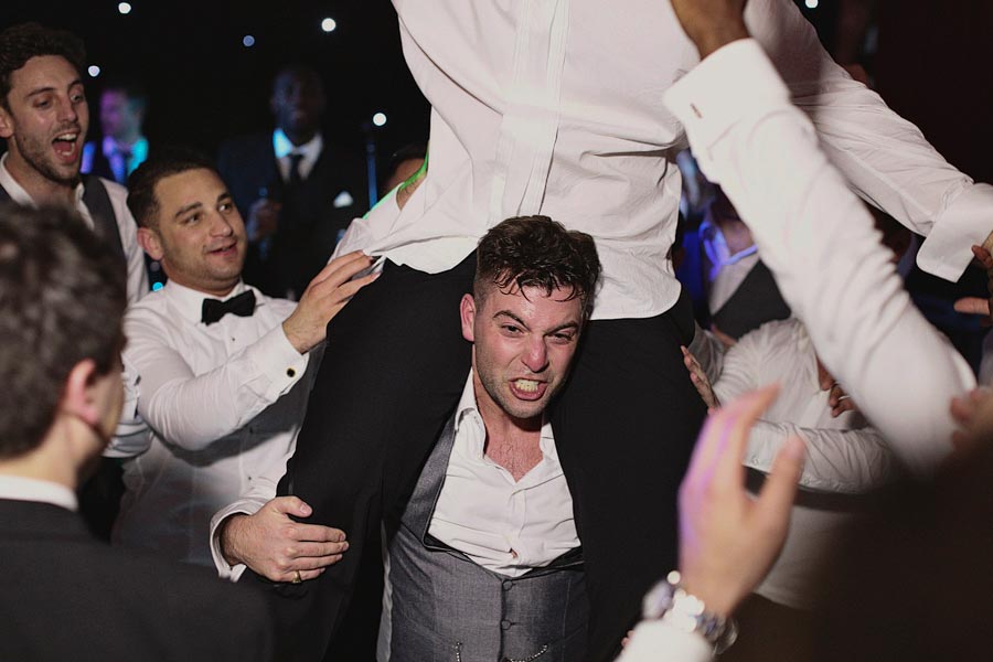 Groom lifted by friends during wedding reception celebration