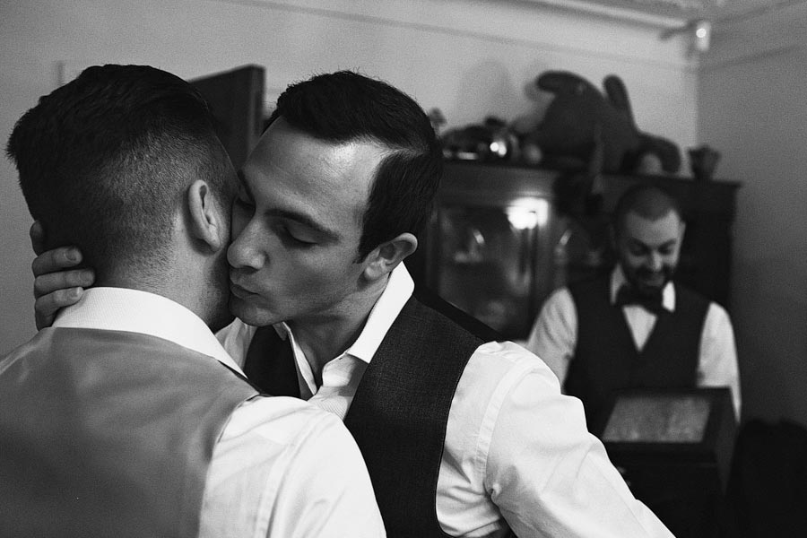 Two men kissing indoors, third man smiling behind.