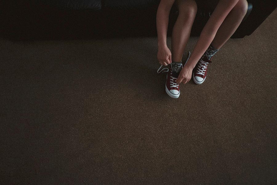 Person tying red sneakers on carpeted floor