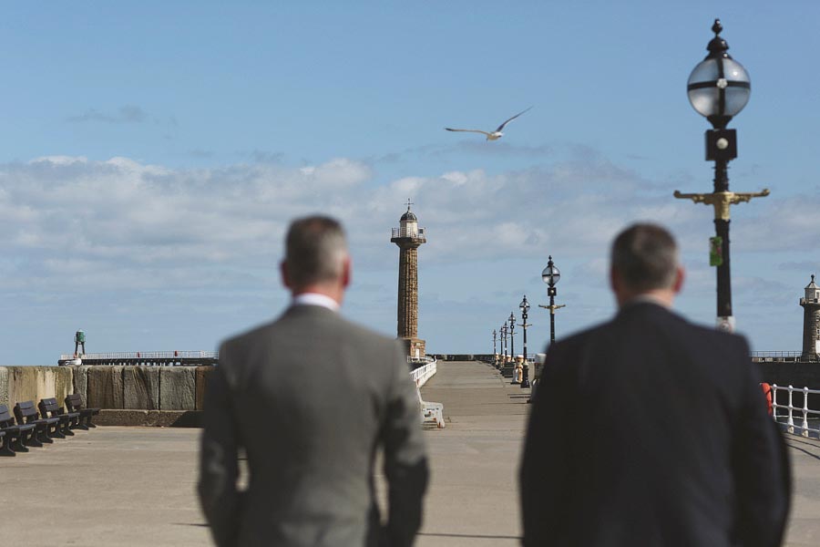 Two men walking toward lighthouse on pier