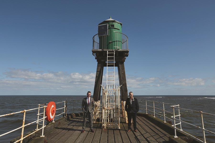 Two men in suits on pier with lighthouse