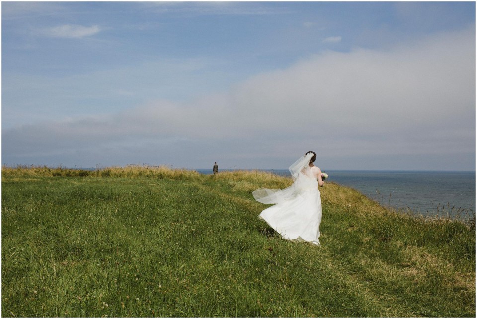 Bride walking on grassy cliff by ocean