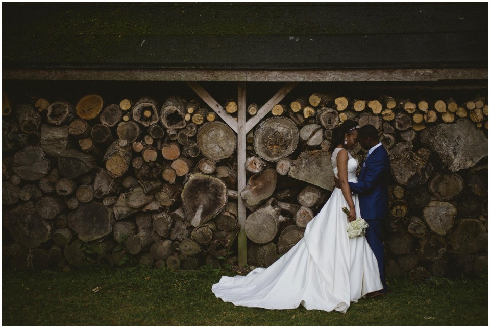 Bride and groom embracing before stacked firewood wall