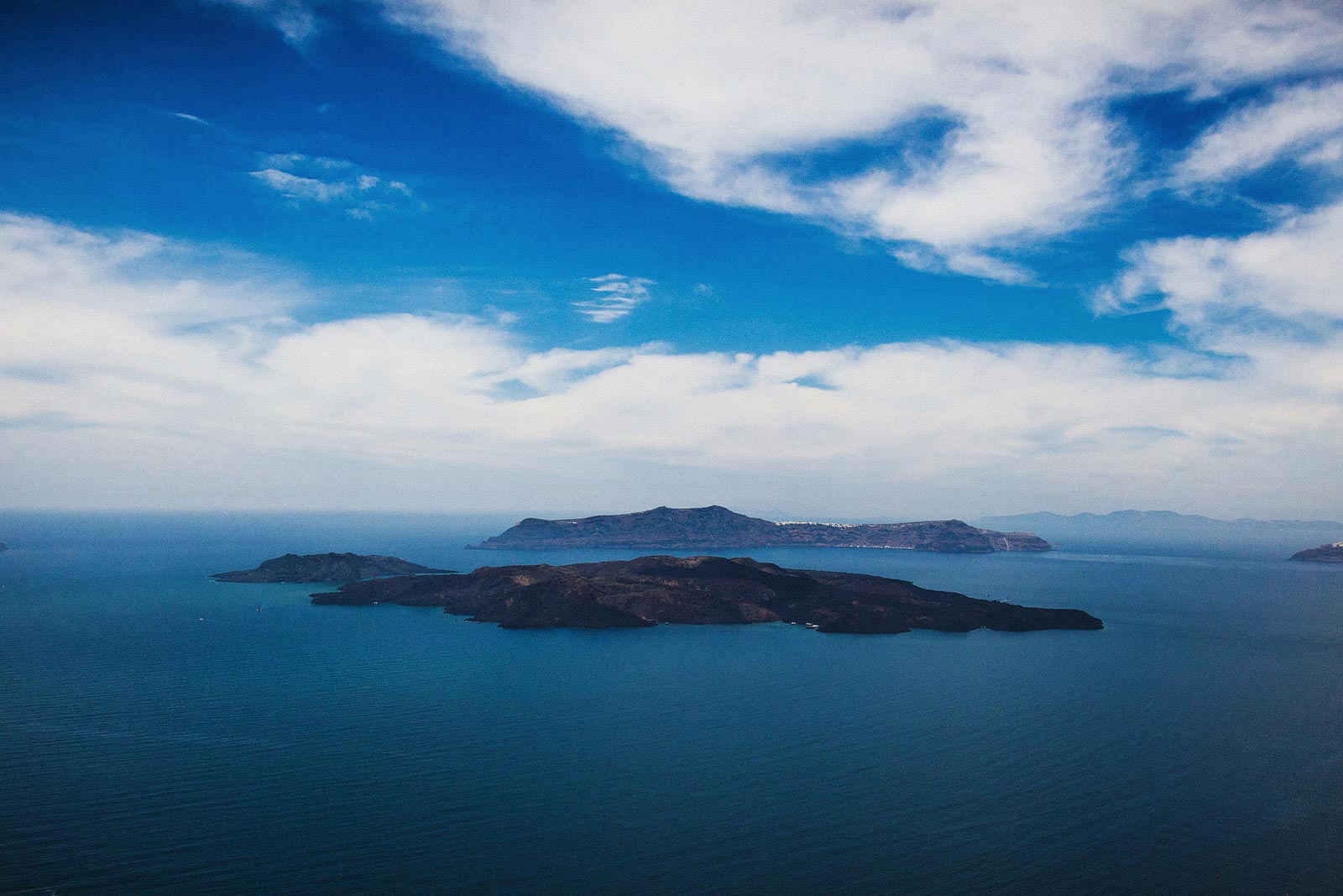 Distant islands rest on calm blue sea beneath wide, cloud-streaked sky.