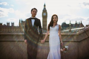 Bride and groom hold hands near Big Ben at sunset, soft light over London skyline, documentary wedding photography.