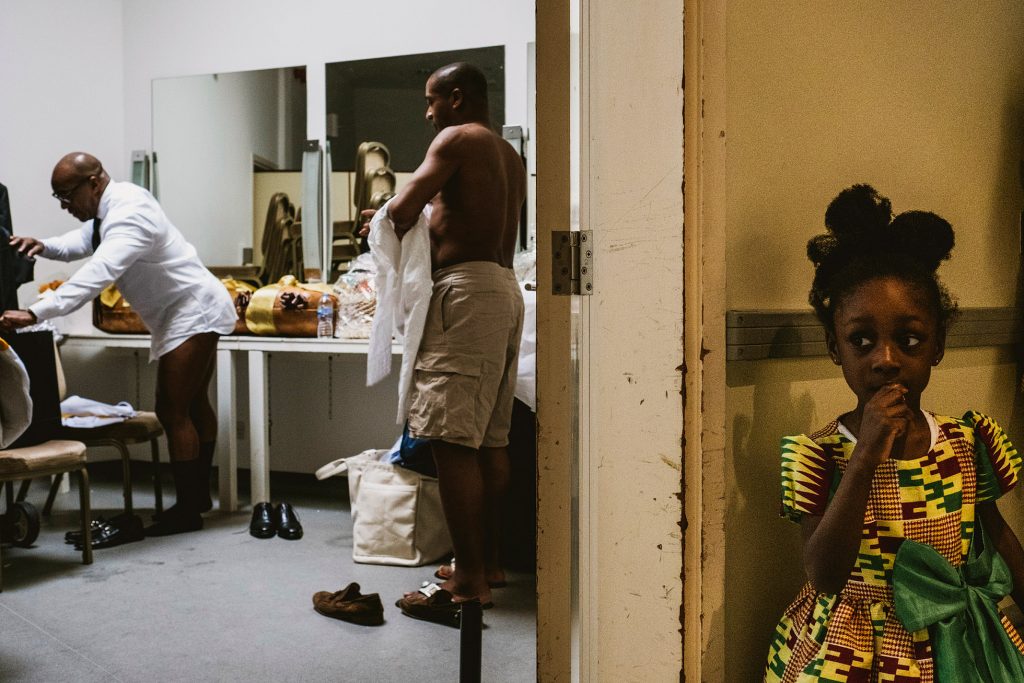 Little girl waits in corridor as men dress in a busy wedding morning changing room.