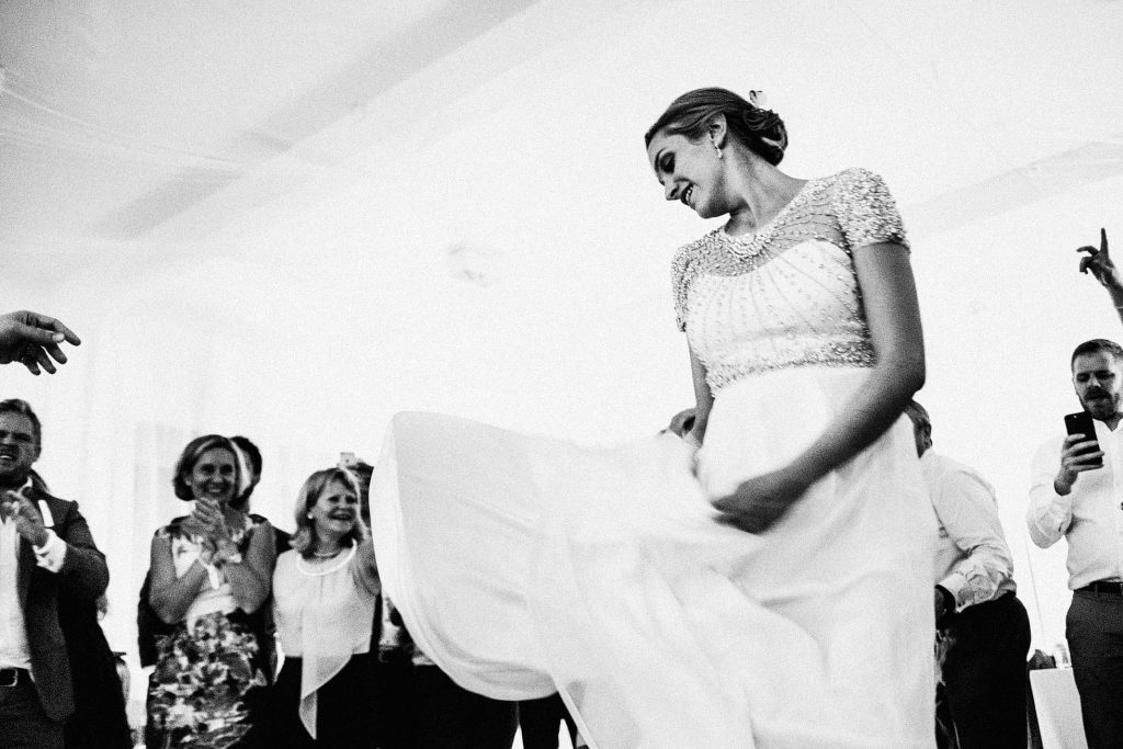 Bride twirls on dance floor as guests clap and smile during documentary wedding photography.