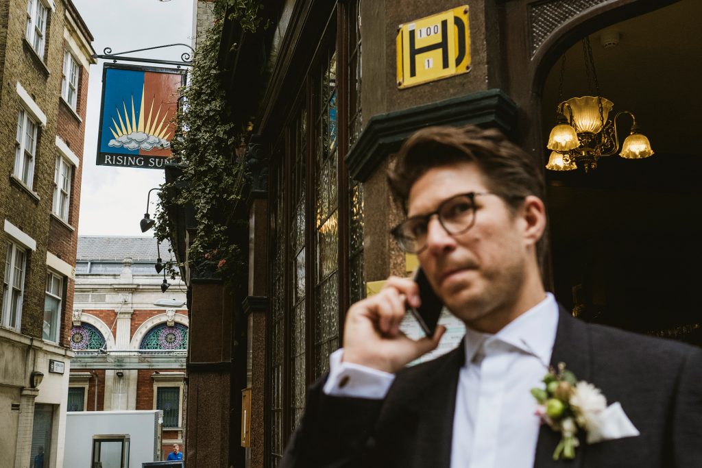 Groom talks on mobile phone on London Street before wedding at the Ned. Photo by York Place Studios