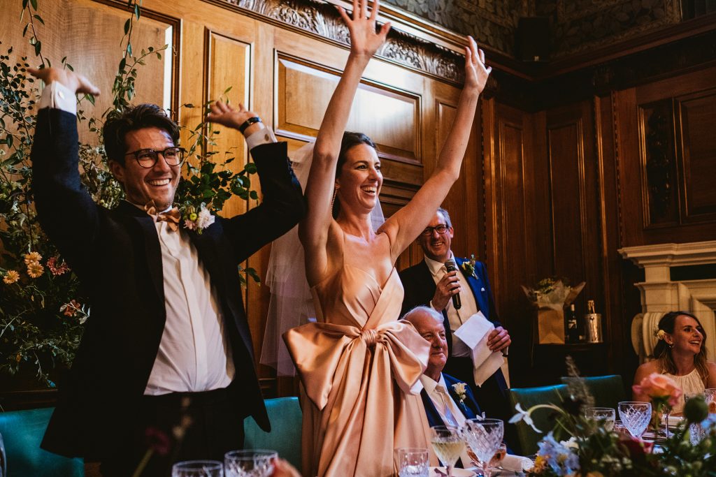 Bride and groom raise their arms laughing during wedding reception speeches.