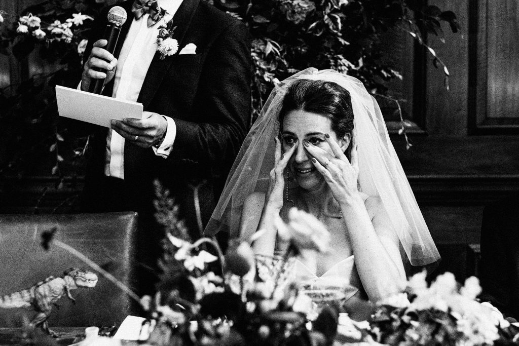 Bride wipes away tears as groom speaks during wedding reception speech.