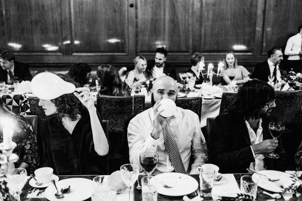 Guests share quiet laughter and wine at a candlelit wedding reception dinner table.