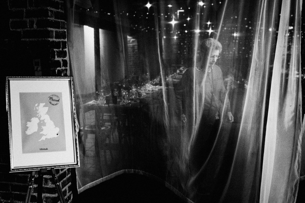 Woman smiling behind sheer curtain at candlelit wedding reception, fairy lights glowing softly.