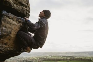 Person climbing a rugged rock face above rolling countryside under a pale sky.