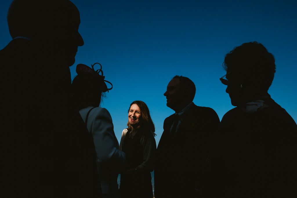 Woman laughing among silhouetted guests against deep blue sky at wedding.