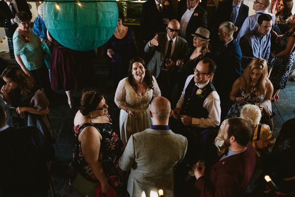 Bride laughing with guests beneath paper lantern at wedding reception.
