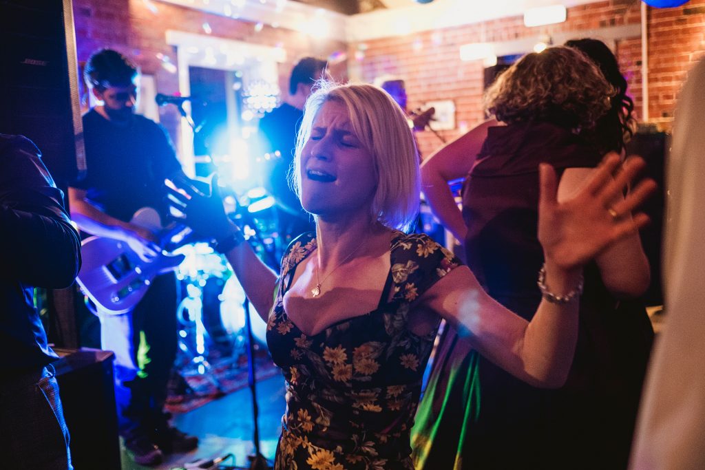 Woman sings with eyes closed, arms wide, as live band plays at wedding reception.