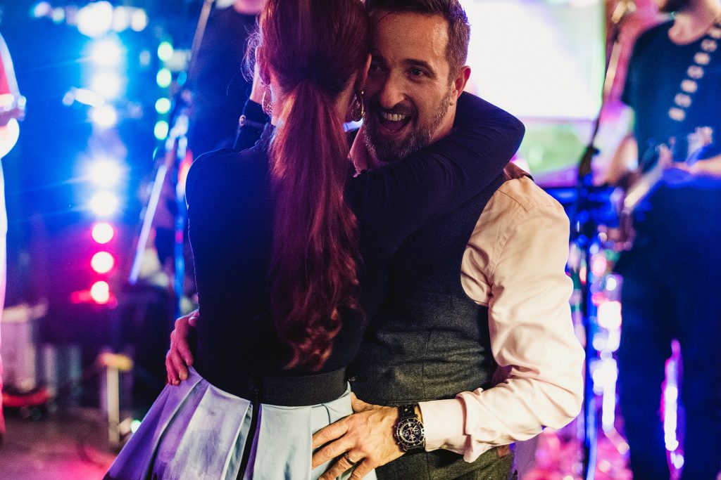 Couple laughing in embrace on colourful wedding reception dance floor.