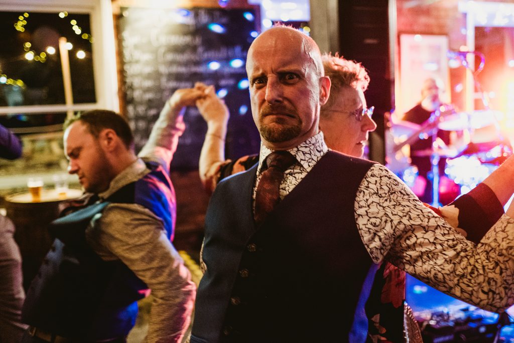 Guests dancing energetically beneath colourful lights at a lively wedding reception.