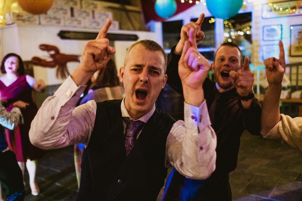 Guests singing with raised hands on a lively wedding reception dance floor.