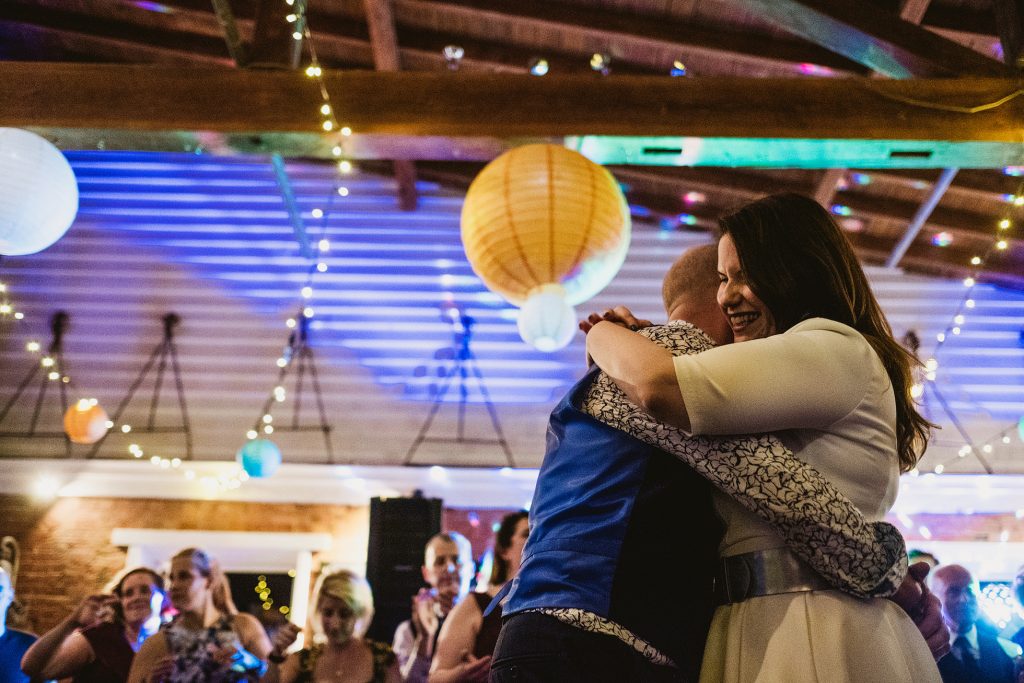 Bride smiling as she hugs guest beneath lanterns at lively wedding reception.
