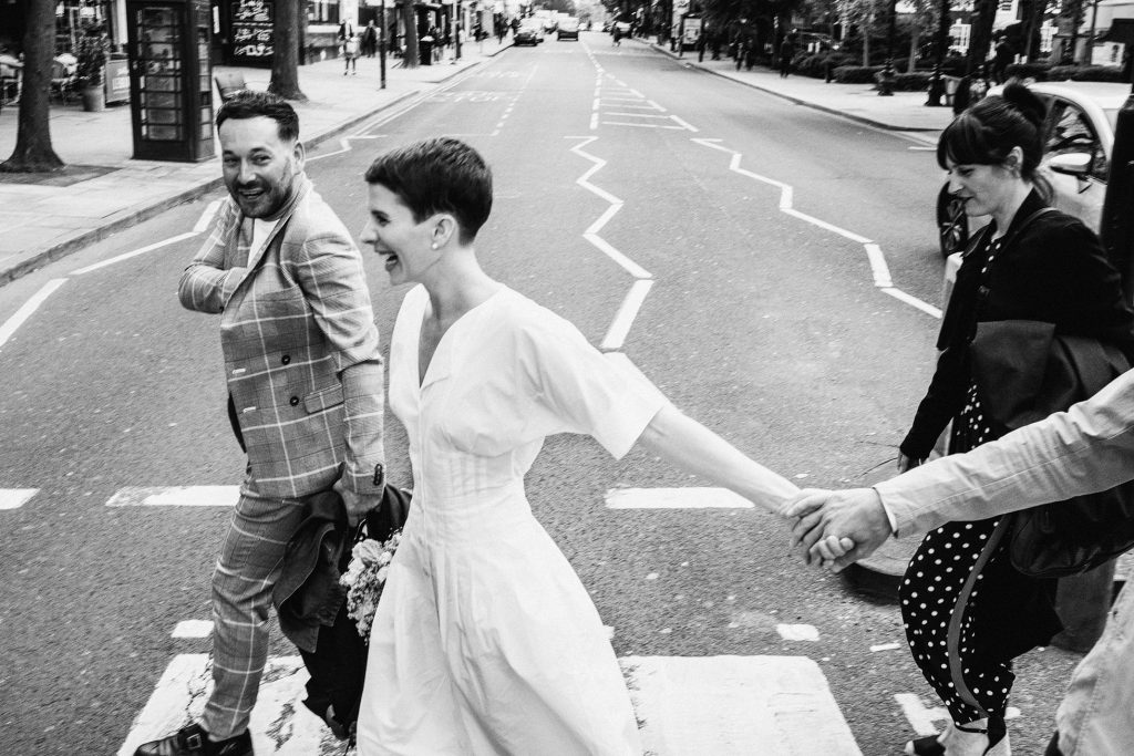 Bride laughing as she crosses city street holding hands, candid documentary wedding photography moment.