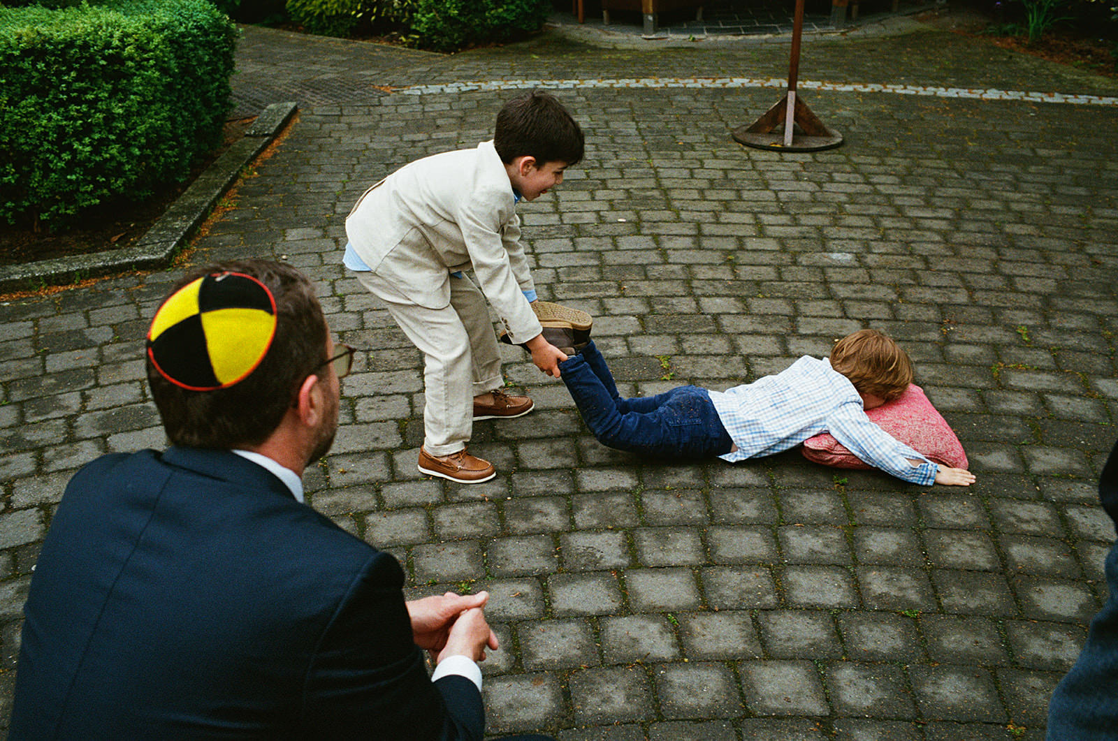Two boys laugh as one pulls the other across cobbles during a wedding celebration.
